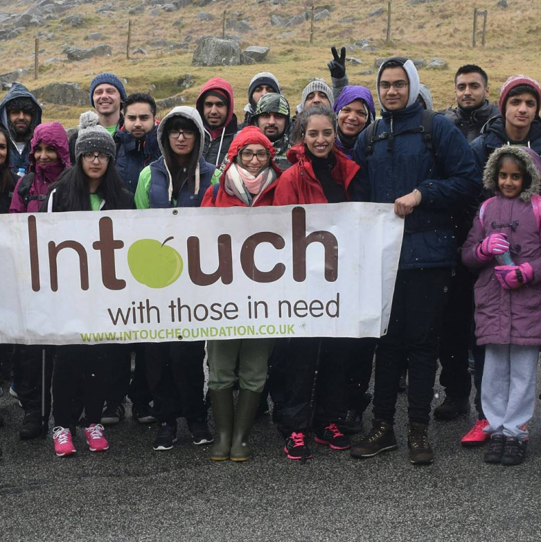 A big group of young adult volunteers lined up outside in winter coats holding a banner with InTouch Foundation written on it, facing the camera
